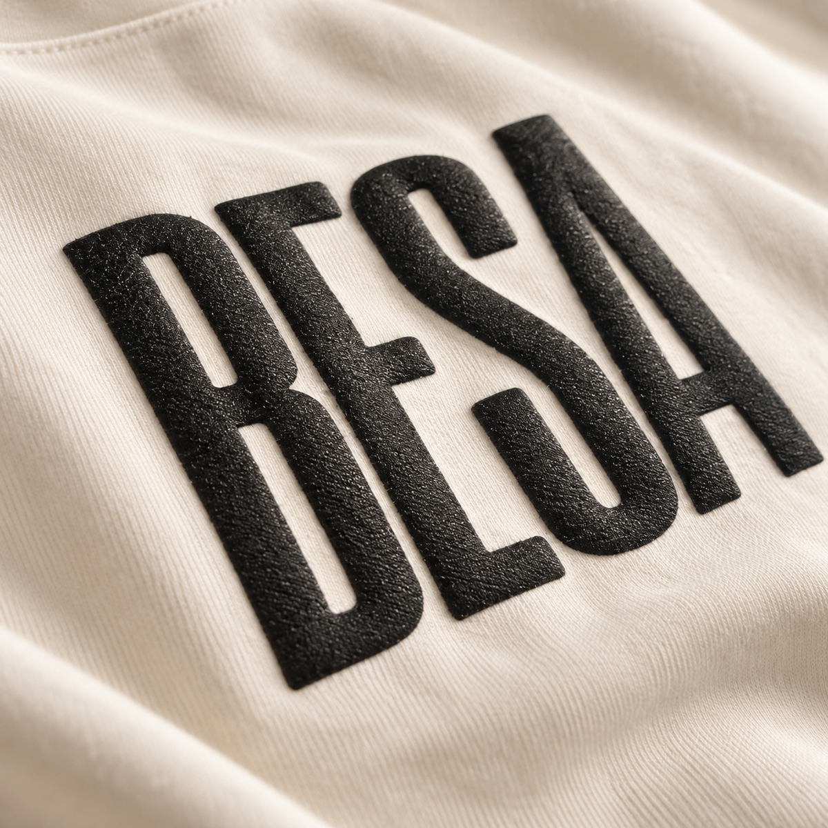 Close-up of textured raised black BESA lettering on ecru fabric.