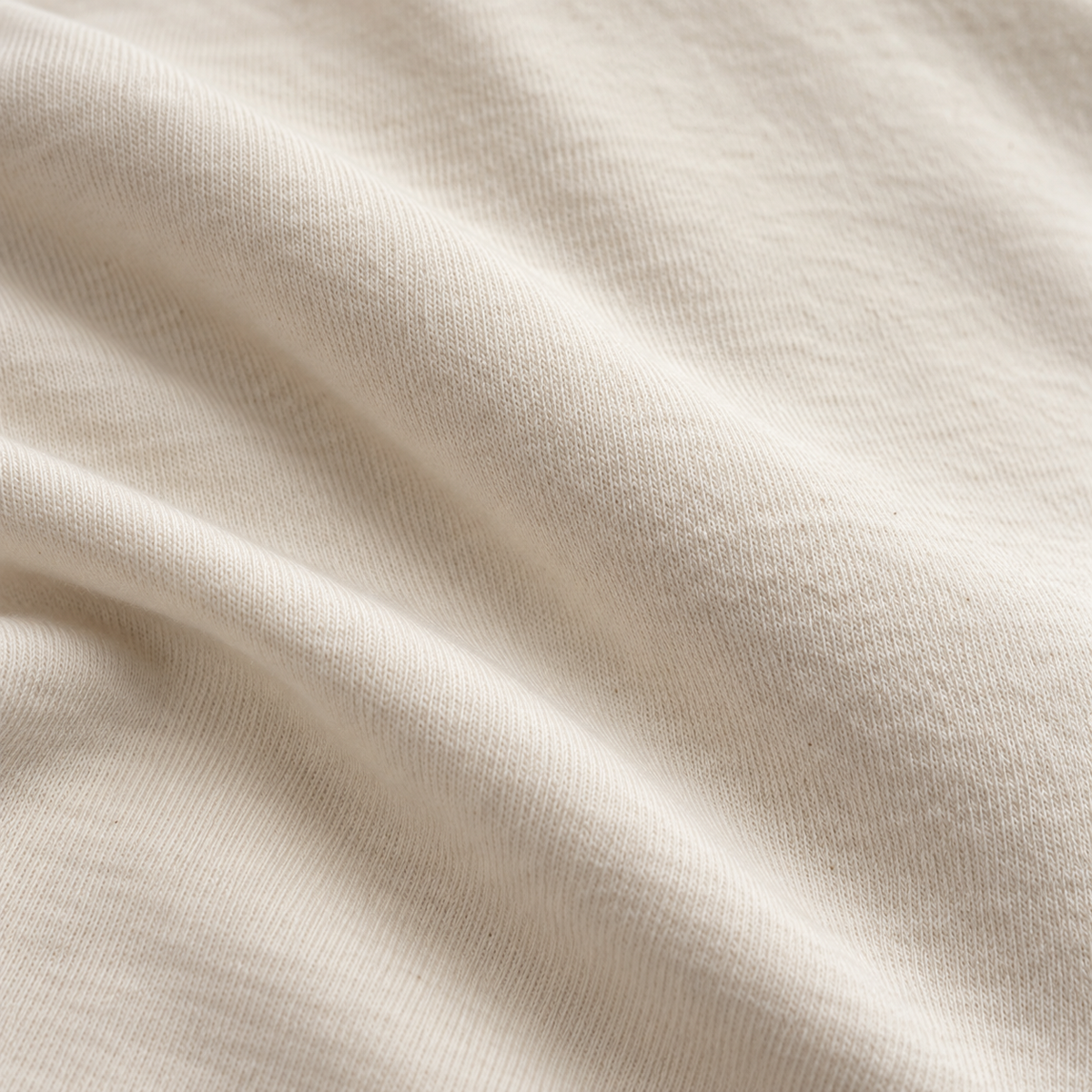 Close-up of softly folded ecru cotton jersey showing the fabric texture.